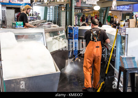 Seattle, Washington, USA - 4. September 2017: männliche Arbeitnehmer tragen ein wasserdichtes Angeln pants ist die Reinigung der Boden bei Pike Place Fish mit einem Druck Stockfoto