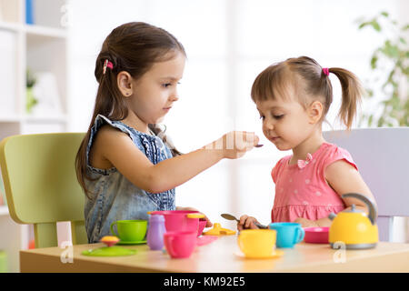 Süße kleine Kinder spielen mit Küchenutensilien beim Sitzen am Tisch zu Hause oder im Kindergarten