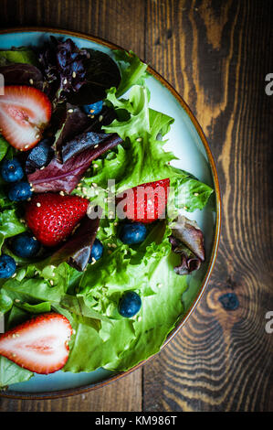 Grüner Salat mit Beeren auf hölzernen Hintergrund Stockfoto