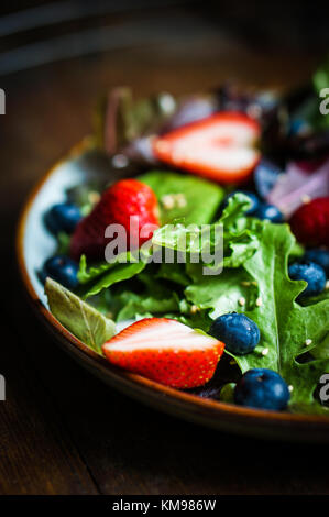 Grüner Salat mit Beeren auf hölzernen Hintergrund Stockfoto