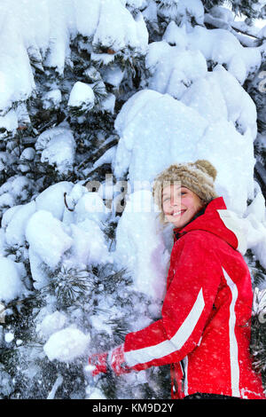 Mädchen mit Winterkleidung schüttelt aus Zweigen der Bäume. Stockfoto