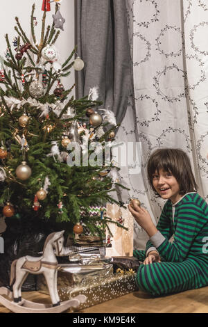 Jungen in seinem Schlafanzug Sitzung durch eine Weihnachtsbaum Stockfoto