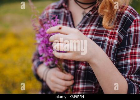 Frau mit Blumen mit einem Marienkäfer auf dem Finger Stockfoto