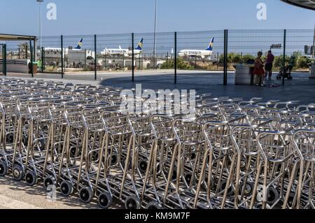 Lange Reihe mit Gepäckwagen am Flughafen Faro in Portugal (Algarve) mit Flugzeugen von Ryanair im Hintergrund. | Nutzung weltweit Stockfoto