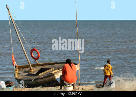 Maputo, Mosambik, Männer sitzen am Strand mit ihrem Boot am Rand Wassers Stockfoto