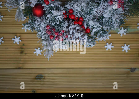 Weihnachten fotografie Bild eines Green Pine Tree Kranz im Schnee mit roten Beeren und rustikal Naturholz Hintergrund Stockfoto