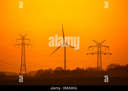 Hochspannung Strommasten/Getriebe Türme und wind turbine gegen Sonnenuntergang Silhouette Stockfoto