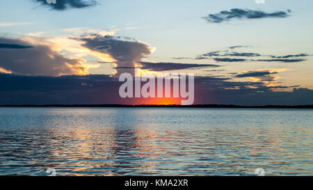 Eine spektakuläre inspirational Bunten trübe Wasser Panoramablick auf das Meer und die Landschaft mit Crimson Sun Glow in Weiß cumulonimbus Cloud für Stockfoto