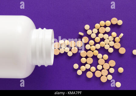 Gruppe der sortierten beige Tabletten. Kapseln verschütten aus weiße Flasche. lila Hintergrund. Stockfoto