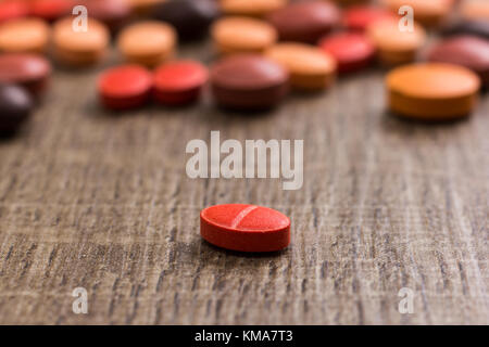 Haufen sortiert orange, braun und rot Kapseln auf hölzernen Tisch. Eine Pille abgesehen ist, isoliert. Stockfoto