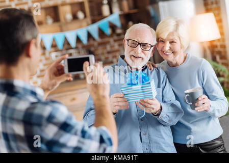 Junger Mann, Foto seiner betagten Eltern holding Geschenk Stockfoto
