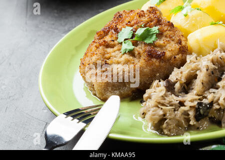 Gebratenes Schweinefleisch Schnitzel mit Salzkartoffeln serviert und gebratene Sauerkraut auf einer Platte Stockfoto