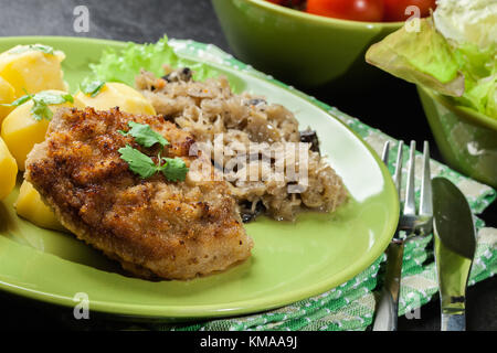 Gebratenes Schweinefleisch Schnitzel mit Salzkartoffeln serviert und gebratene Sauerkraut auf einer Platte Stockfoto