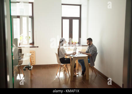 Friedliche achtsame Geschäftsfrau, die Yoga-Meditation am Schreibtisch praktiziert, während Geschäftskollege arbeitet Stockfoto
