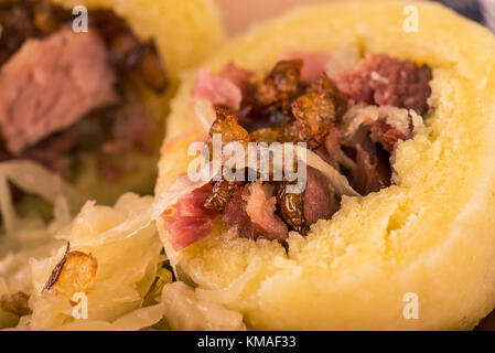 Horizontale Foto von einem Teil der kartoffelklöße von geräuchertem Schweinefleisch gefüllt. Saurer Kohl ist neben Mahlzeit auf Lehm Platte. Stücke von gebratenen Zwiebeln ein Stockfoto