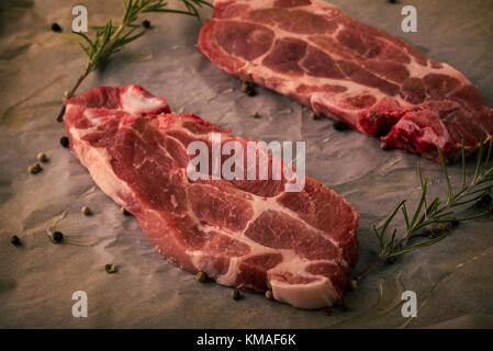 Horizontale Foto von zwei Scheiben Schweinekamm Steaks. Das Fleisch Teile mit roter Farbe und Fett auf abgenutzten Backen Blatt Papier mit Pfeffer platziert ist, rose Stockfoto