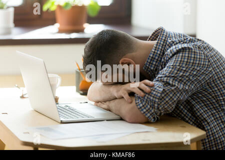Müder Manager, der an einem harten Arbeitstag im Heimbüro über dem Laptop schläft. Erschöpfter Schlaf beraubt gestresste männliche Arbeiter, die auf Tisch liegen und schlafen Stockfoto
