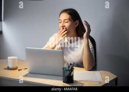 Erschöpfte Millennials-Geschäftsfrau in Freizeitkleidung gähnt am Arbeitsplatz im Home Office. Die müde junge Arbeitgeberin will abends bei der Arbeit schlafen Stockfoto