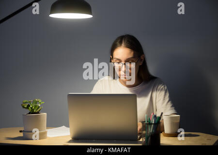 Portrait der tausendjährigen Geschäftsfrau in Gläsern auf Laptop suchen und Arbeiten bei Nacht. Konzentrierte weibliche Manager mit Computer im Home Office in e Stockfoto