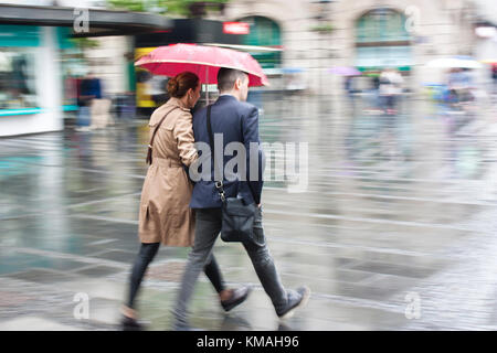 Belgrad, Serbien - Mai 5, 2017: Der junge Mann und die Frau zu Fuß in Eile unter dem Dach an regnerischen und blurry city street Stockfoto