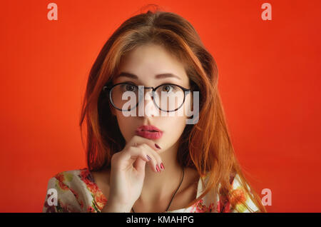 Porträt eines emotionalen kaukasische Mädchen in Gläsern im Elfenbeinturm Kleid mit Blumen auf dem roten Hintergrund. Konzeptionelle studio Foto einer jungen Modell Stockfoto