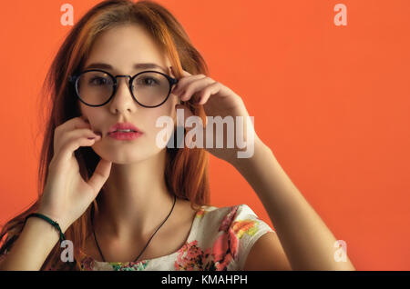 Porträt einer der schönsten kaukasische Mädchen in Gläsern im Elfenbeinturm Kleid mit Blumen auf dem orangen Hintergrund. Konzeptionelle studio Foto einer jungen cheerfu Stockfoto