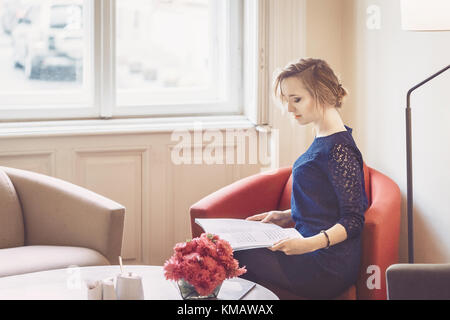 Schöne Frau ist lesen Magazin im Sessel sitzen Stockfoto