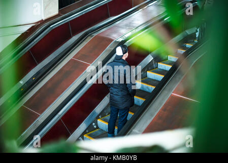 Rückansicht Mann bewegte sich auf der Rolltreppe in der u-bahn Rolltreppe in der U-Bahn. nach oben Treppe. elektrischer Rolltreppe. Blick durch das Grün. Selektive Weichzeichner. Stockfoto