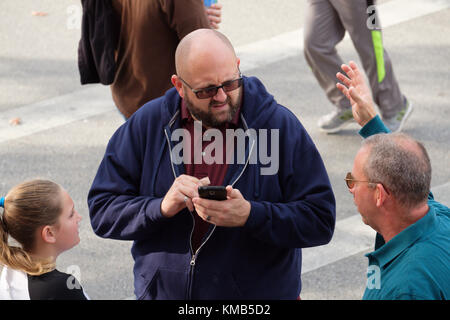 Mann auf der Straße halten Smartphone Handy und im Gespräch mit einem anderen Mann und junge Mädchen Stockfoto