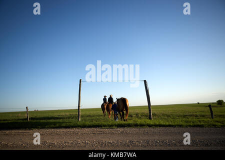 Cowboys Position heraus auf den Bereich in den Abend mit einem Sonnenuntergang Glühen am Horizont und der Mann an der Rückweg führt sein Pferd durch die Zügel Stockfoto