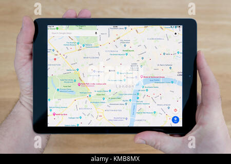Ein Mann schaut auf der Google Maps Website auf seinem iPad tablet device, Schuß gegen einen hölzernen Tisch top Hintergrund (nur redaktionelle Nutzung) Stockfoto