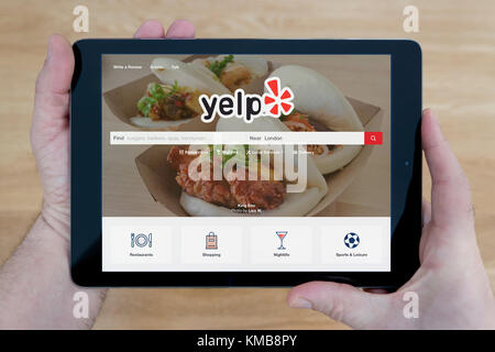 Ein Mann schaut auf die Website von Yelp auf seinem iPad tablet device, Schuß gegen einen hölzernen Tisch top Hintergrund (nur redaktionelle Nutzung) Stockfoto