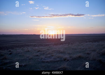 Sonnenaufgang über frosty Feld mit verdorrten Gras im Herbst. orange Sun steigt mehr als gerade Linie von fernen Horizont Stockfoto