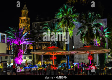 Eine bunte Sidewalk Cafe auf der Promenade Riva Promenade in Split Kroatien spät in der Nacht mit Palmen, Sonnenschirmen und Turm beleuchtet mit Leds Stockfoto