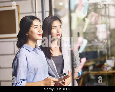 Zwei junge asiatische Unternehmer zusammengetan, um die Analyse der Geschäftssituation mit Haftnotizen und digitale Tablet-PC im Büro. Stockfoto