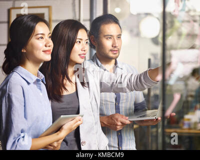 Drei junge asiatische Unternehmer zusammengetan, um die Analyse der Geschäftssituation mit Laptop Computer, digitale Tablet und Haftnotizen im Amt. Stockfoto