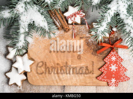 Weihnachten Grußkarte: Gebrannt Worten "Frohe Weihnachten!" auf Holzbrett mit Xmas Tree Zweige, Schnee, Spielzeug und süßen xmas Cookies eingerichtet Stockfoto