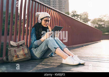 Single Asien student Suche Informationen online mit einem Tablett in der Straße vor dem Universitätsgebäude sitzen. Stockfoto