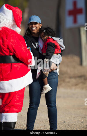 Kinder warten gespannt auf die Ankunft des Weihnachtsmannes, als er aus der Drop-Zone während der 20th Annual Randy Oler Memorial Operation Toy Drop geht, veranstaltet von U.S. Army Civil Affairs & Psychological Operations Command (Airborne), Dez. 01 2017. Die Operation Toy Drop ist die größte kombinierte Luftoperation der Welt mit neun teilnehmenden Partnernationsparatroopern und ermöglicht Soldaten, ihre militärische Berufsspezialität zu trainieren, ihre Luftbereitschaft aufrechtzuerhalten und der lokalen Gemeinschaft etwas zurückzugeben. (USA Armee Stockfoto