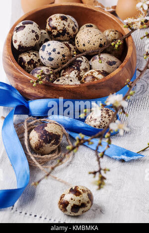 Hölzerne Schüssel von der Wachtel Eier mit Blüte Zweig und blauen Klebeband über Grau textile Serviette Stockfoto