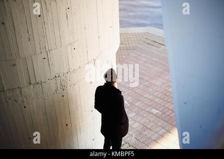 Junge Mann in einem schwarzen Mantel, der an das Wasser und in die Ferne schaut Stockfoto