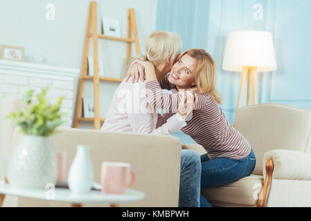 Liebevolle Großmutter sitzt auf einem Sofa, während eine Enkelin umarmte ihre Stockfoto