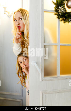 Foto von Mutter und Tochter lugen hinter Tür mit Weihnachten Kranz Stockfoto