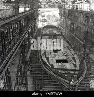 1950er Jahre, historische Bild eines Schiffes im Bau in einem trockendock unter dem Arrol Gantry an der berühmten Harland und Wolff Werft, wo die Titanic und anderen großen Olympischen - Kategorie Schiffe gebaut wurden, Belfast, Nordirland. Stockfoto