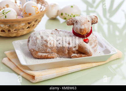 Schöne traditionelle Ostern lanb Kuchen mit Puderzucker, Korb voller Ostereier im Hintergrund Stockfoto