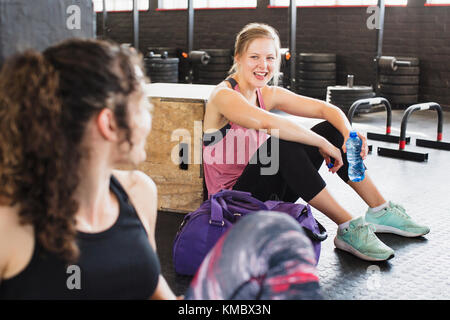 Lächelnde junge Frauen ruhen und Trinkwasser nach dem Training in Fitnessraum Stockfoto