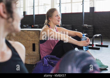 Lächelnde junge Frau Ruhe und Trinkwasser nach dem Training in Fitnessraum Stockfoto