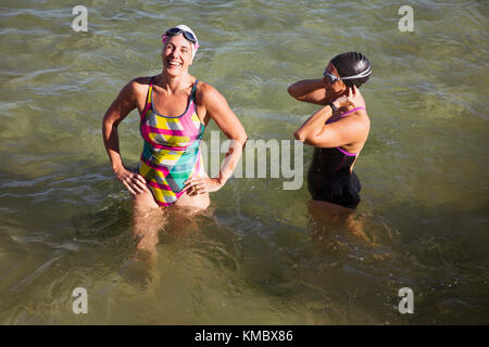 Lachende weibliche Schwimmer im offenen Wasser watend in sonnigen Ozean Stockfoto