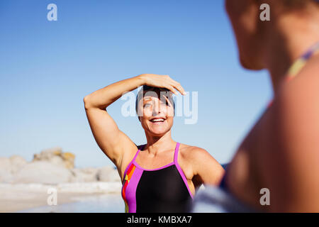 Lächelnde weibliche Schwimmer am sonnigen Strand Stockfoto