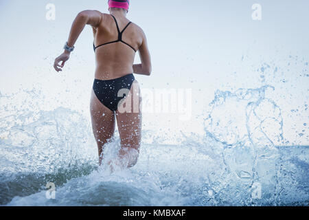 Weibliche Open water Schwimmer laufen und Planschen in Ocean Surf Stockfoto